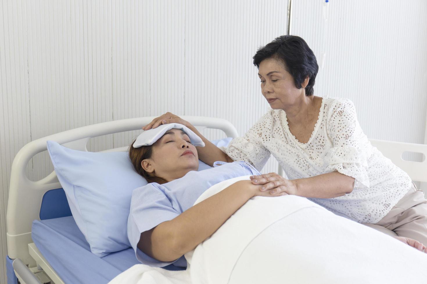 een Aziatische moeder zorgt voor haar zieke dochter op een ziekenhuisbed. foto