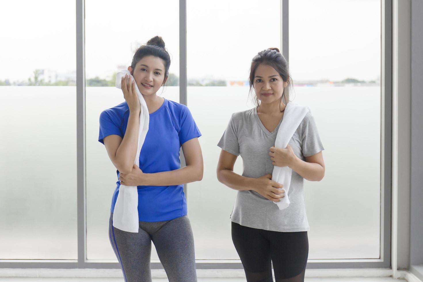 twee Aziatische vrouwen van middelbare leeftijd rusten uit en gebruiken een zweethanddoek na het sporten in de fitnessruimte. foto