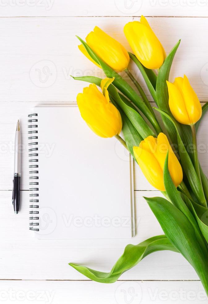 mooie gele tulpen, lege papieren notitieblok op witte houten achtergrond. foto