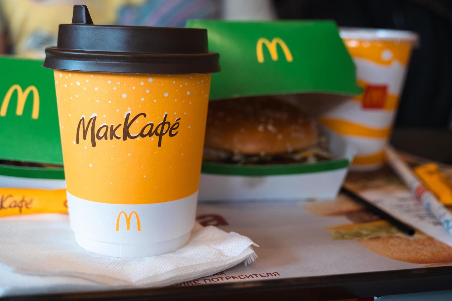 een papieren kopje mcdonald's koffie met het opschrift maccafe in het russisch en een hamburger in een doos op een dienblad. fastfoodrestaurantketens. Rusland, Kaluga, 21 maart 2022. foto