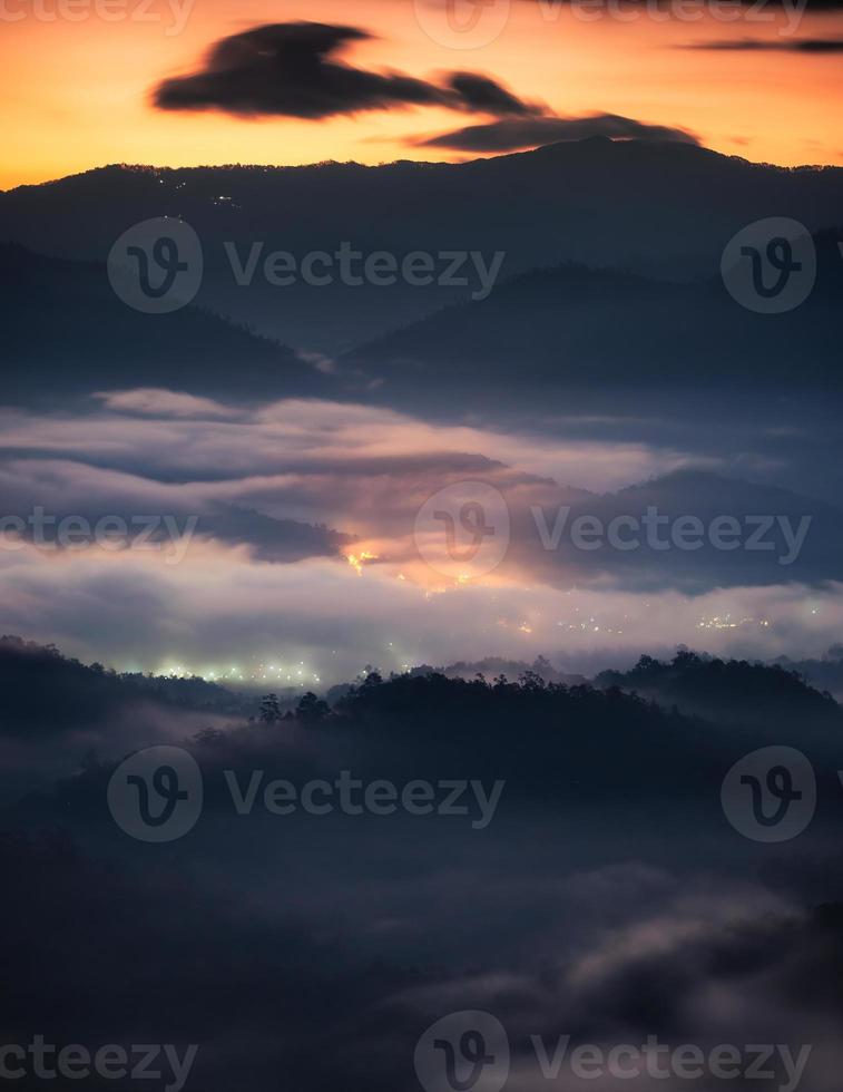 landschap van bergketen en mistig stromend op heuvel met verlichte stad in de vallei foto