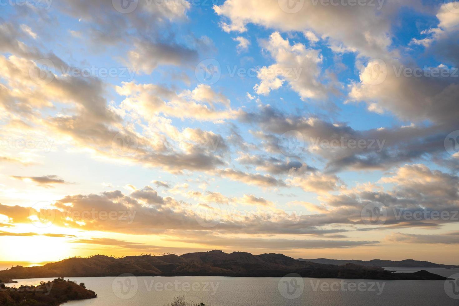 prachtige zonsondergang aan zee met heuvels en zon die onder wolkenlucht naar beneden komen foto