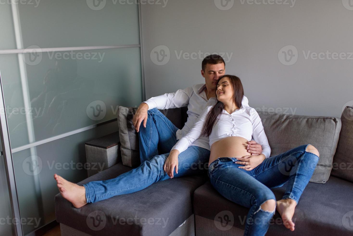 een man en een zwangere vrouw zitten knuffelend op de bank. foto
