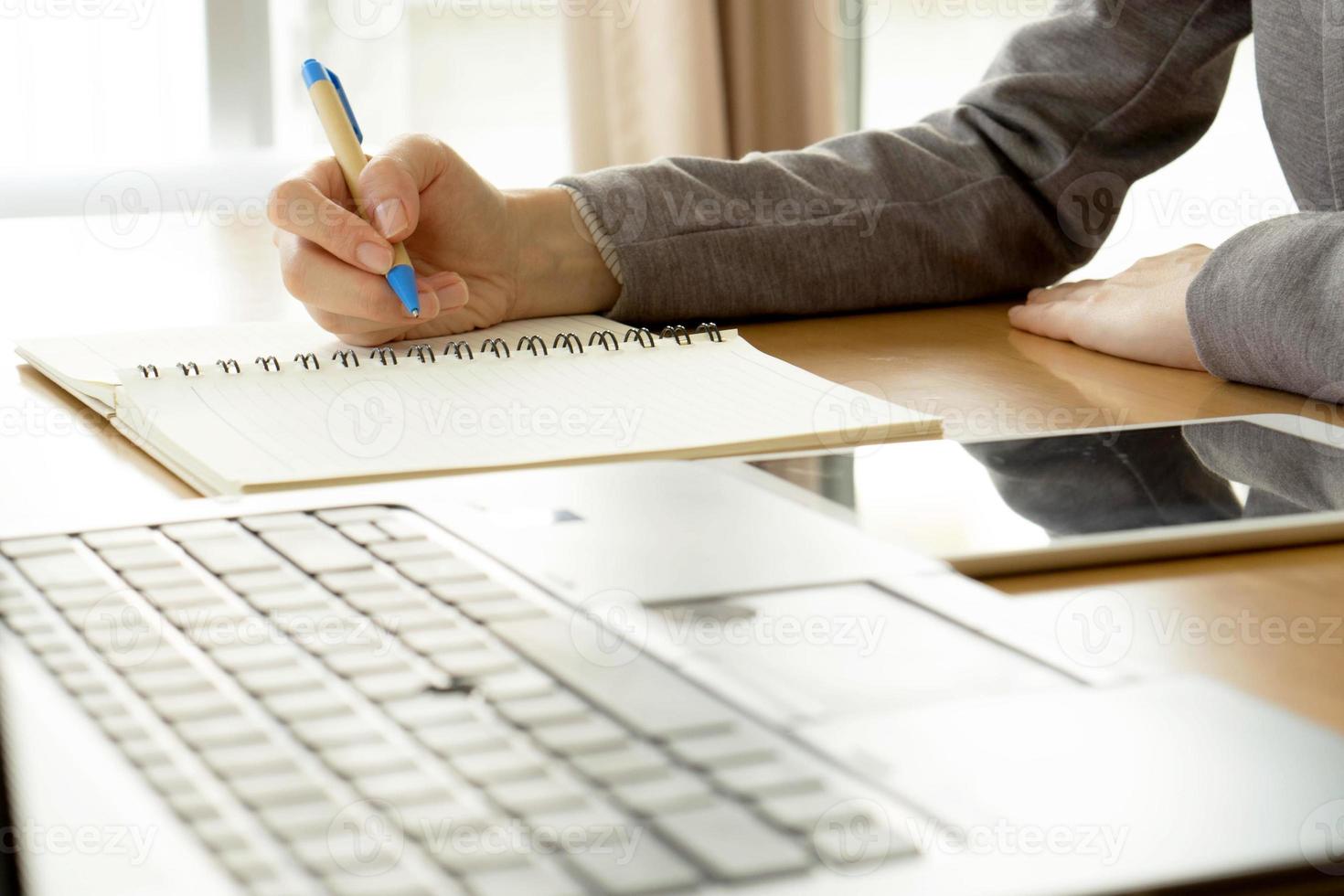 close-up werkende vrouw schrijven op papier en typen op laptopcomputer in kantoorruimte foto