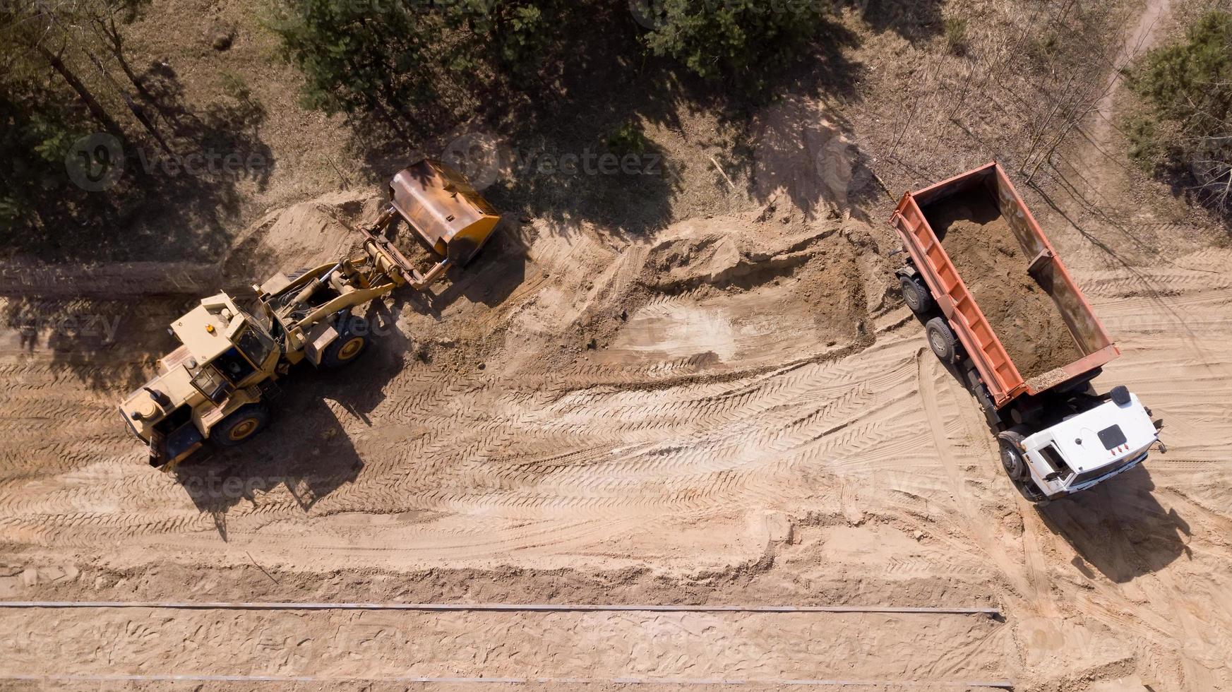 de lader laadt het zand in de vrachtwagen. reparatie van wegen. het uitzicht vanaf de top foto