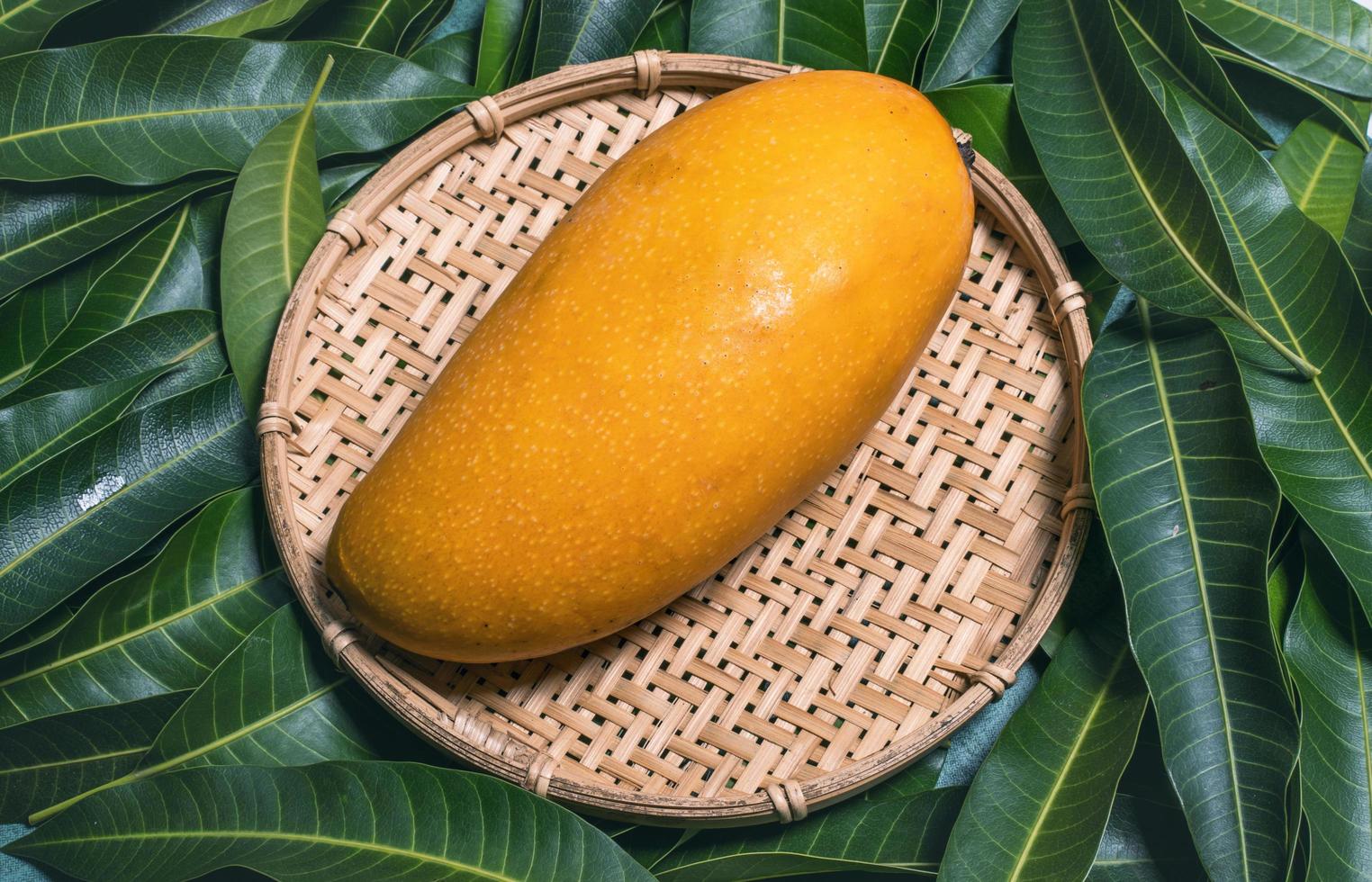 vers sappig mooi mangofruit in bamboezeef over groene bladachtergrond. tropisch zomeroogstconcept, bovenaanzicht, close-up, macro, kopieerruimte. foto