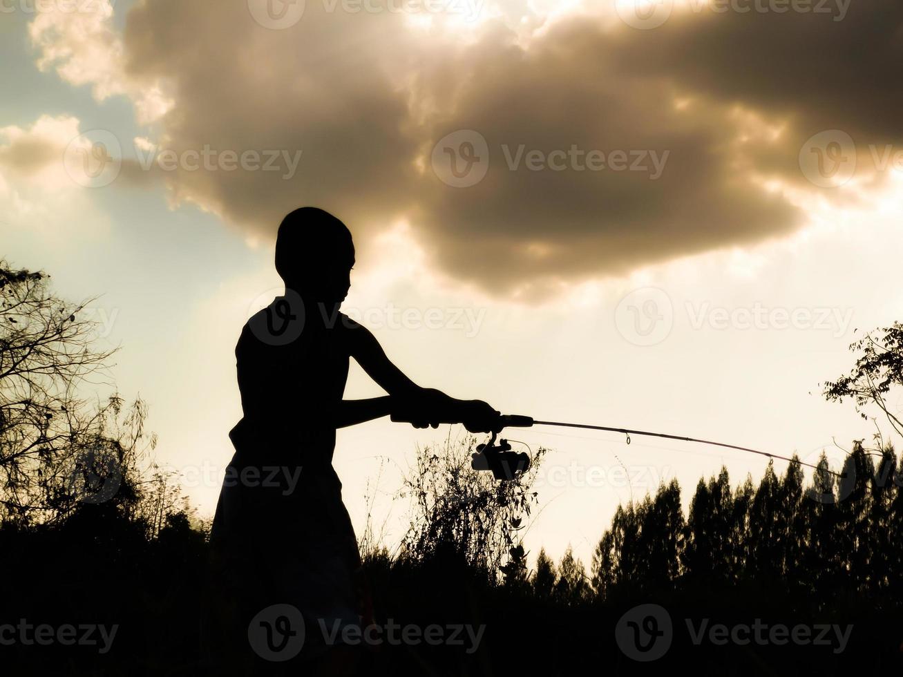 silhouet van een kind dat de gelukkige tijd van kinderen vist midden in de natuur bij zonsondergang foto