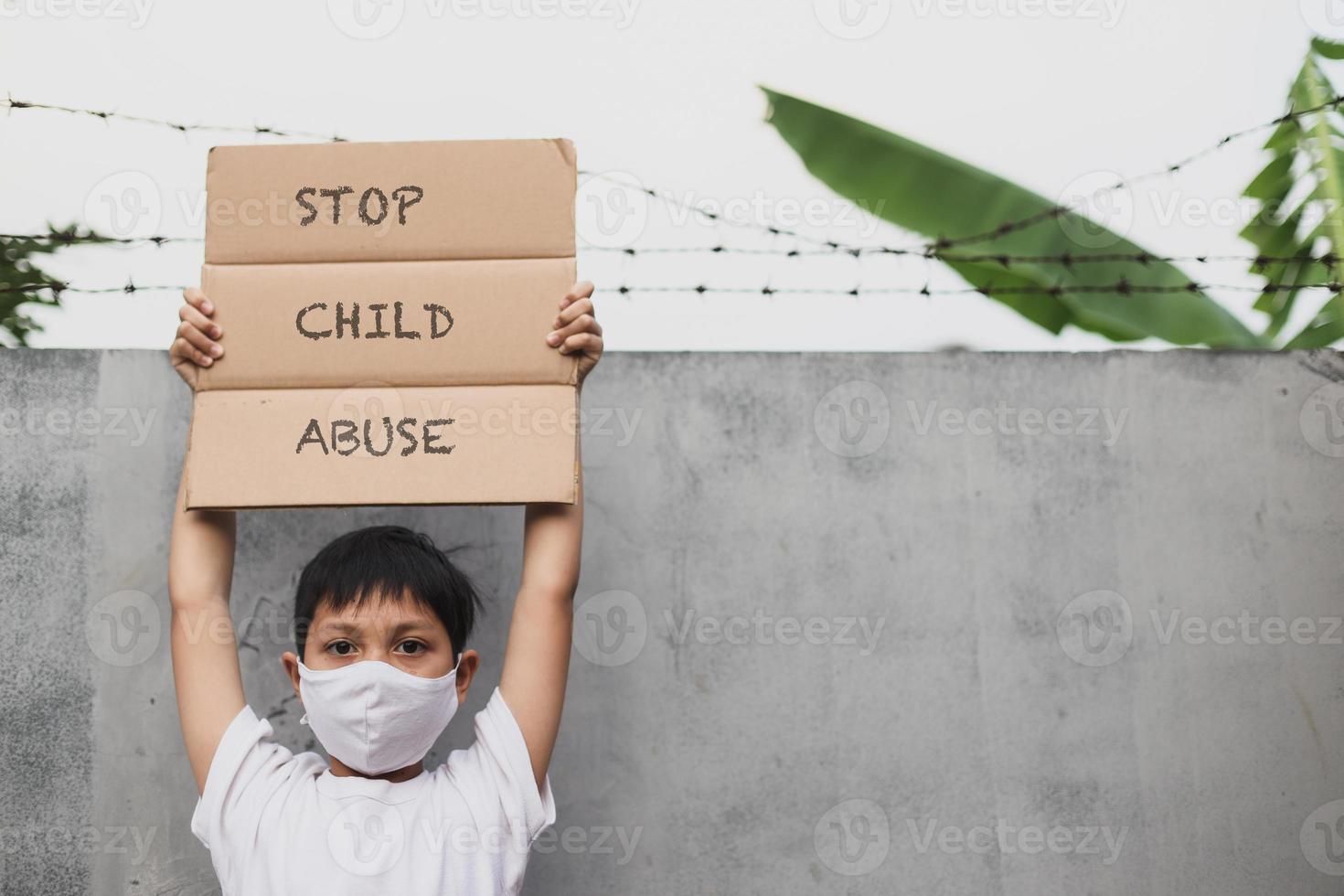 Aziatische jongen voert campagne met een beschermend masker terwijl hij het briefbord opheft en zegt: stop kindermishandeling foto