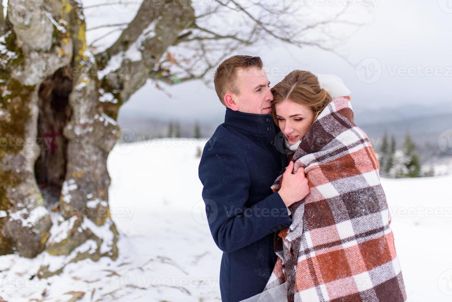 de bruidegom leidt zijn bruid bij de hand naar een eenzame oude beuk. winterse bruiloft. plaats voor een logo. foto