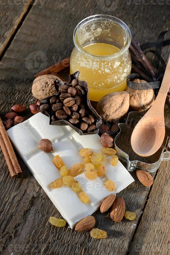 houten lepel met honing op een houten tafel naast tegels van witte chocolade, rozijnen, kaneelstokjes foto