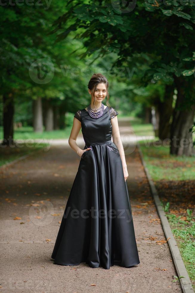 jonge mooie vrouw poseren in een zwarte jurk in een park. foto