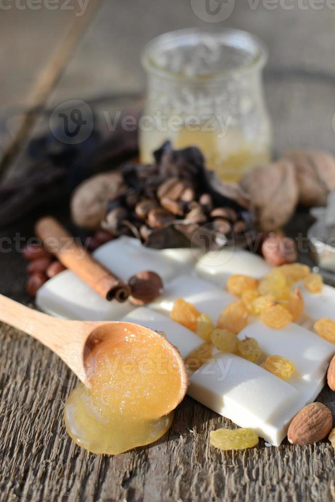 houten lepel met honing op een houten tafel naast tegels van witte chocolade, rozijnen, kaneelstokjes foto