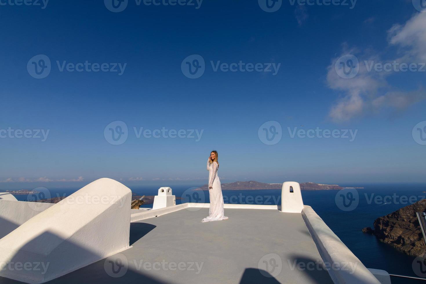 mooie bruid in een witte jurk die zich voordeed op het dak van het huis tegen de achtergrond van de middellandse zee in thira, santorini. foto