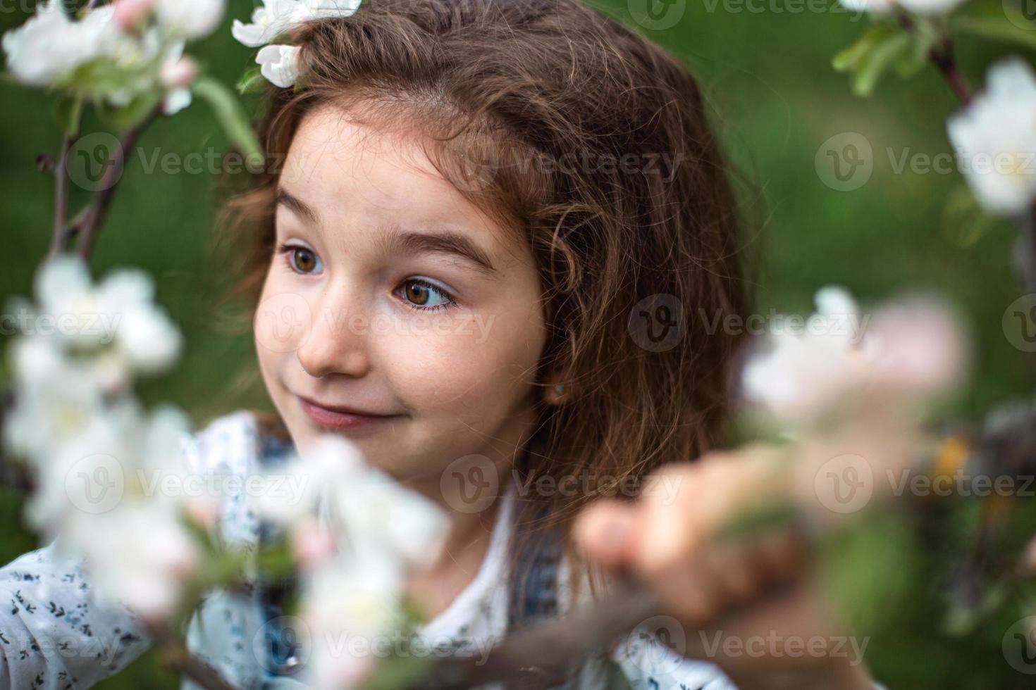 een schattig klein meisje van 5 jaar oud in een bloeiende witte appelboomgaard in het voorjaar. lente, boomgaard, bloei, allergie, lentegeur, tederheid, zorg voor de natuur. portret foto