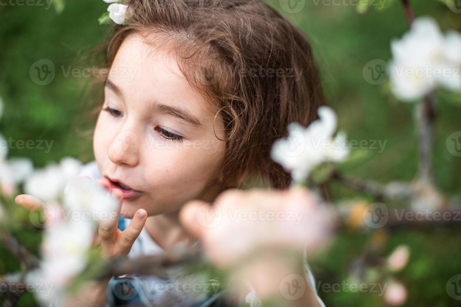 een schattig klein meisje van 5 jaar oud in een bloeiende witte appelboomgaard in het voorjaar. lente, boomgaard, bloei, allergie, lentegeur, tederheid, zorg voor de natuur. portret foto