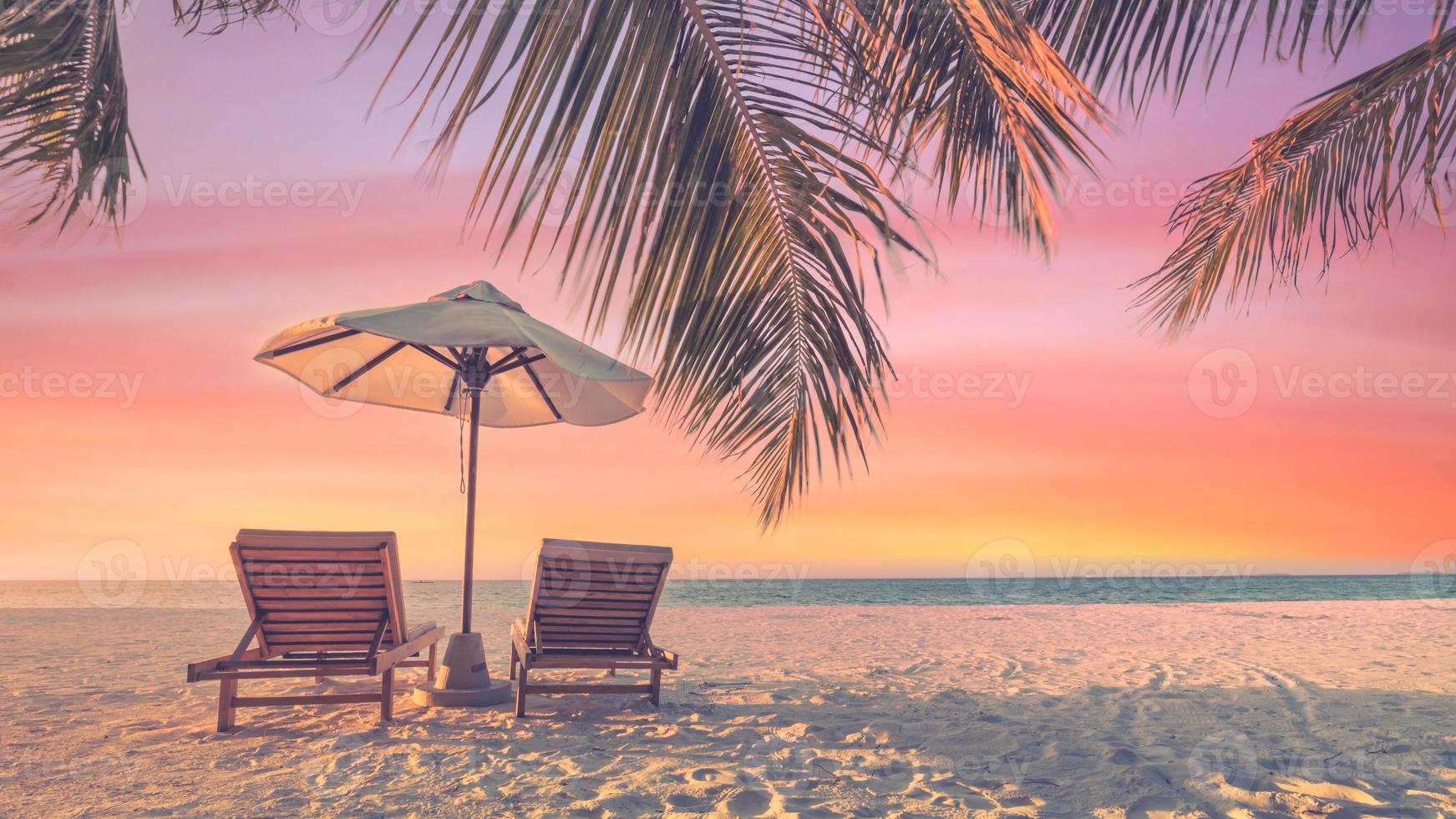 prachtig tropisch zonsonderganglandschap, twee ligbedden, ligstoelen, parasol onder palmboom. wit zand, uitzicht op zee met horizon, kleurrijke schemerhemel, rust en ontspanning. inspirerend strandresorthotel foto