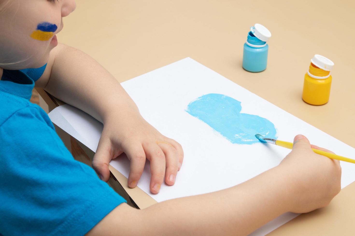 gele en blauwe verf en kinderhanden met een penseel aan tafel. tekeningen van Oekraïens kinderconcept foto