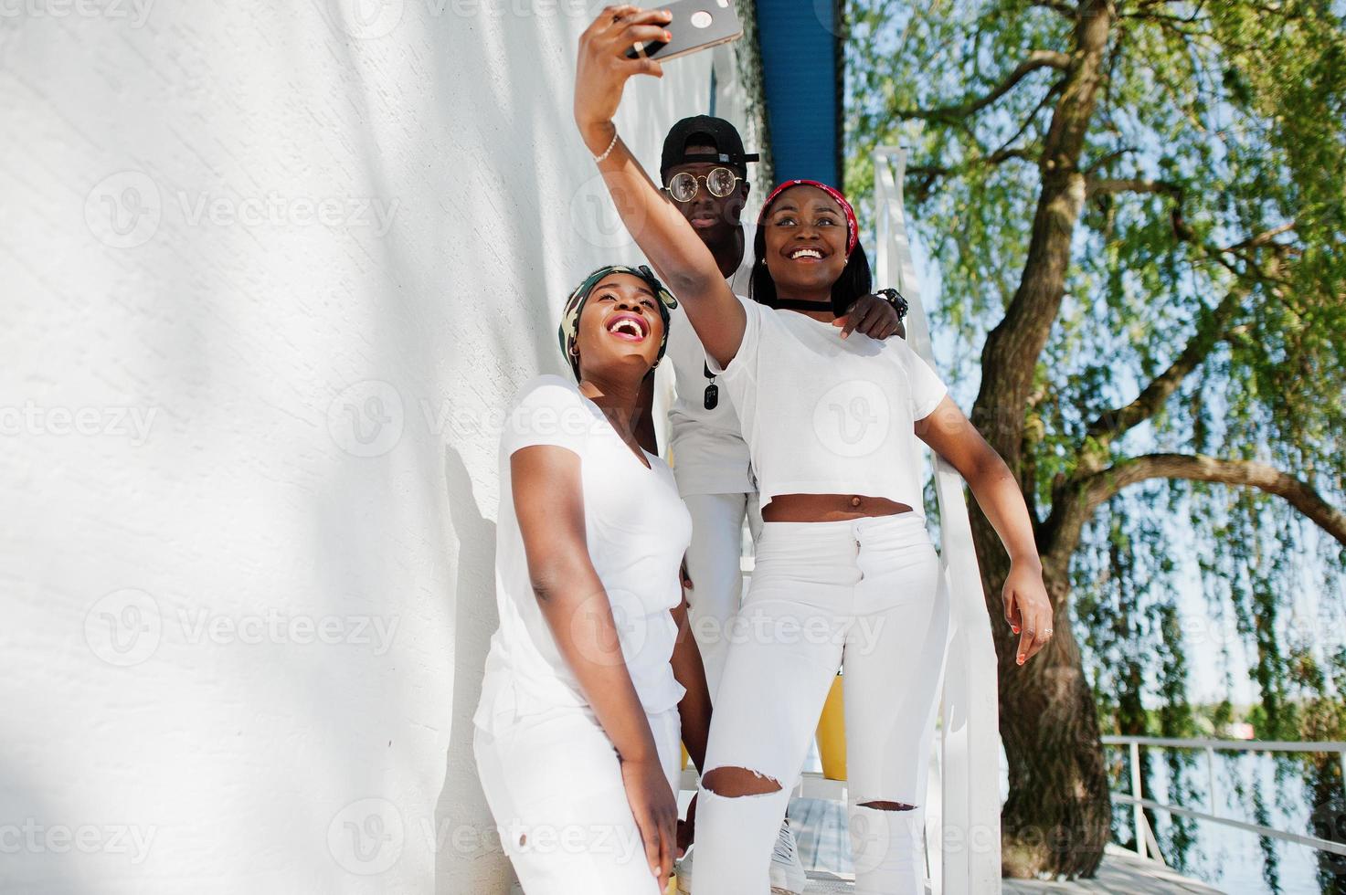 drie stijlvolle afro-amerikaanse vrienden, draag witte kleren die selfie maken. straatmode van jonge zwarte mensen. zwarte man met twee Afrikaanse meisjes. foto