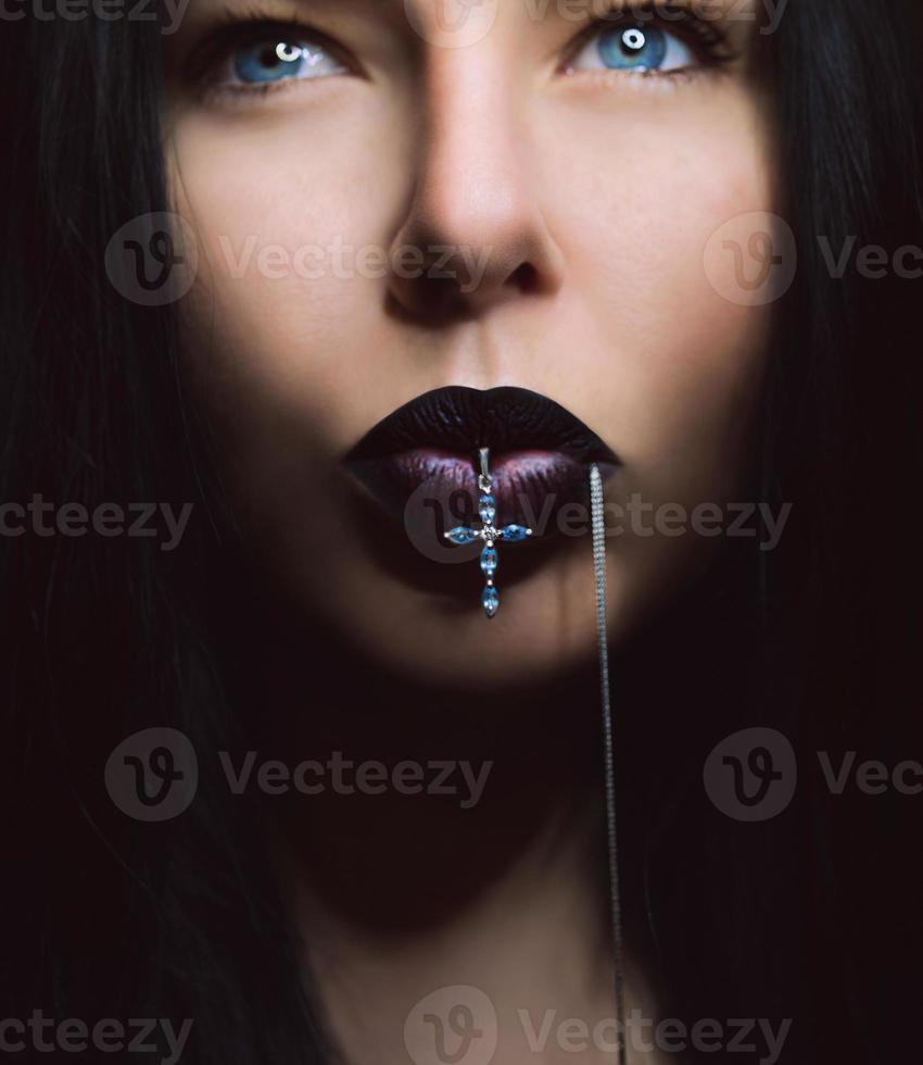 portret van donker haar vrouw met donkere lippen met kruis in haar mond foto