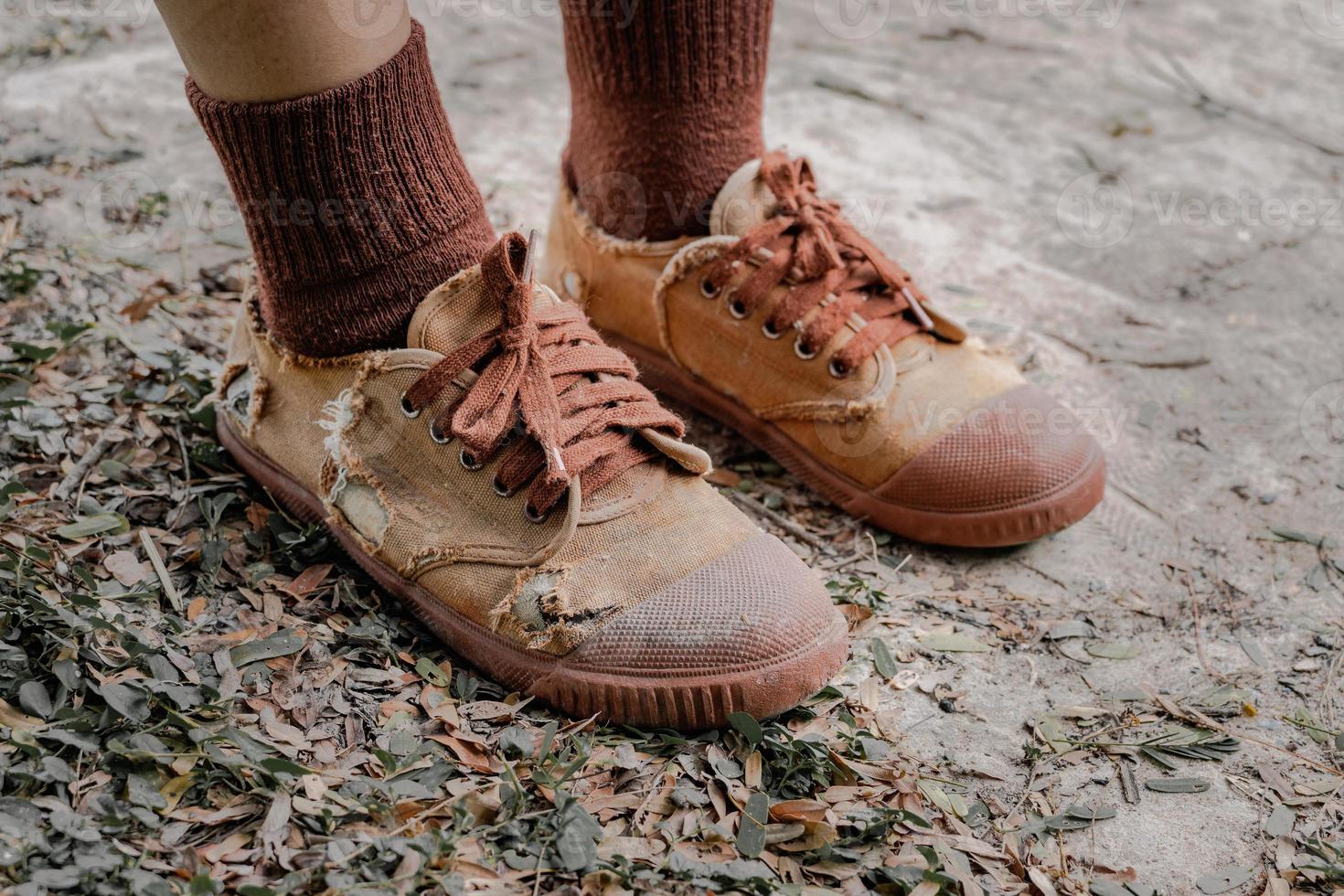 gescheurde studentenschoenen, armoede van scholieren op het platteland kunnen zich vaak geen nieuwe schoenen veroorloven, middelbare scholierenbenen die gescheurde schoenen dragen, armzalig tekort aan onderwijsmateriaal, versleten bruine oude sneakers foto