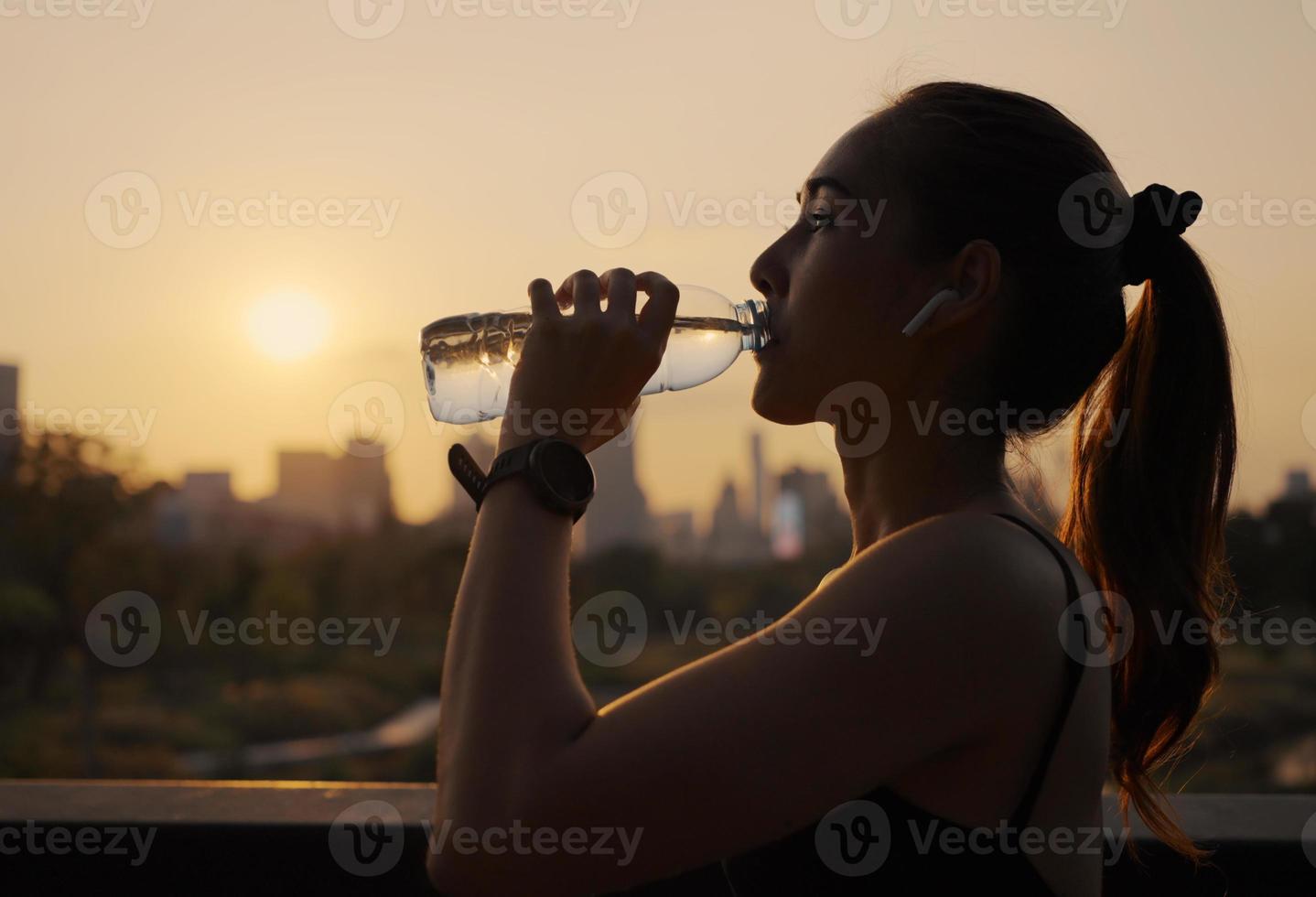 jonge vrouw drinkwater na het joggen bij zonsondergang. foto