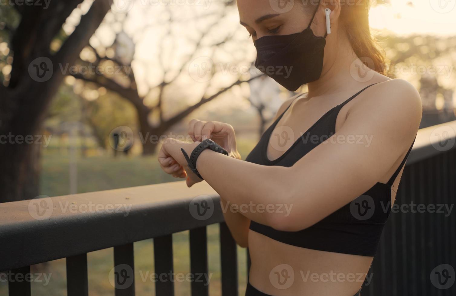 vrouw die een beschermend masker draagt en het fitness slimme horloge opzet om te rennen. sportvrouw die horlogeapparaat controleert. foto