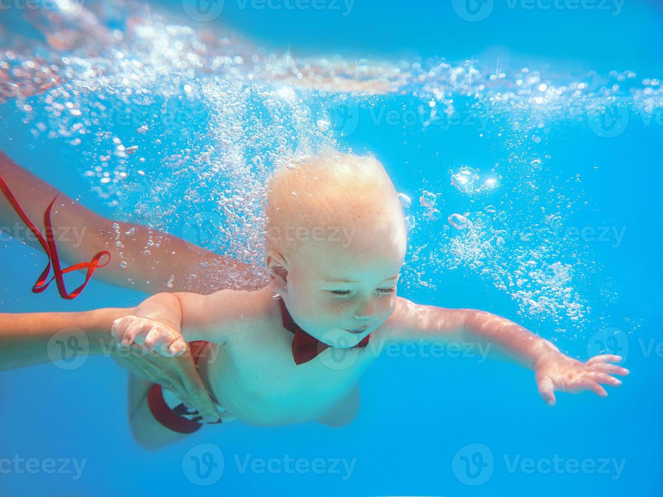 kleine jongen baby met rode vlinder onderwater duiken in het zwembad, leren zwemmen. sport en vakantie concept foto