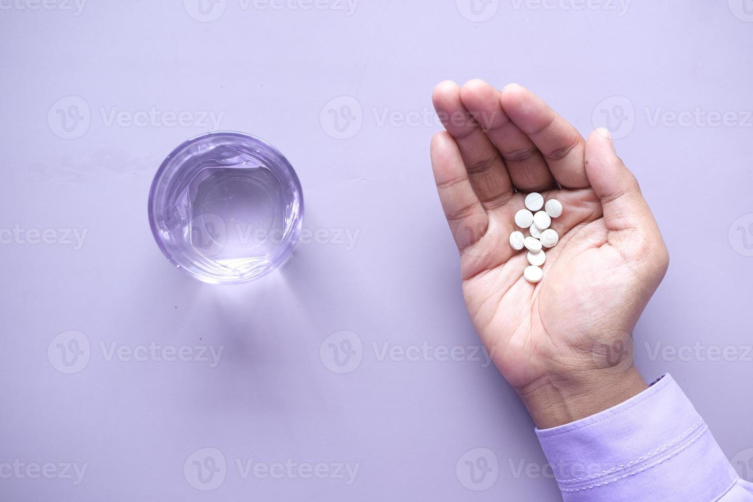 bovenaanzicht van pillen bij de hand met glas water op paarse achtergrond foto