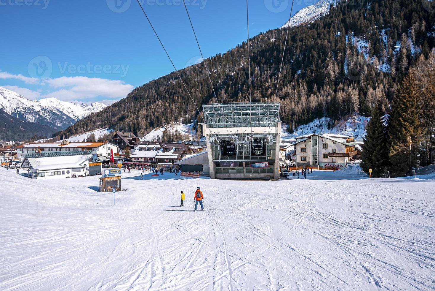 skiërs skiën naar station op besneeuwde berg in alpen met dicht bos foto