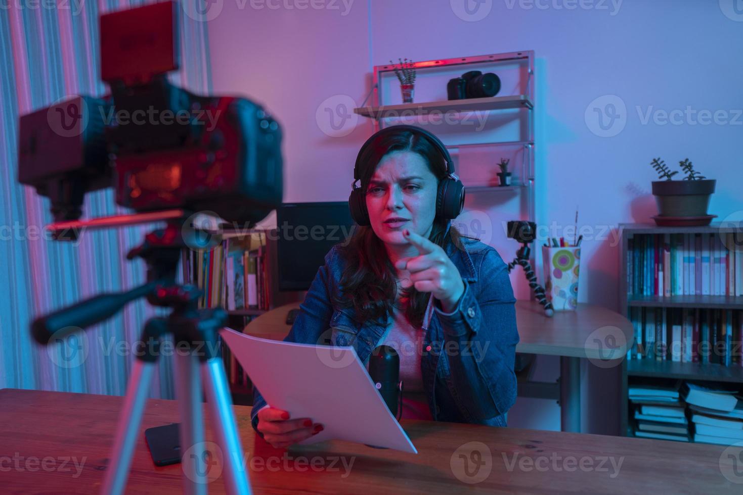 mooie Spaanse vrouw voor een videocamera die een blog opneemt in haar studio met rode en blauwe lichten in haar huis foto