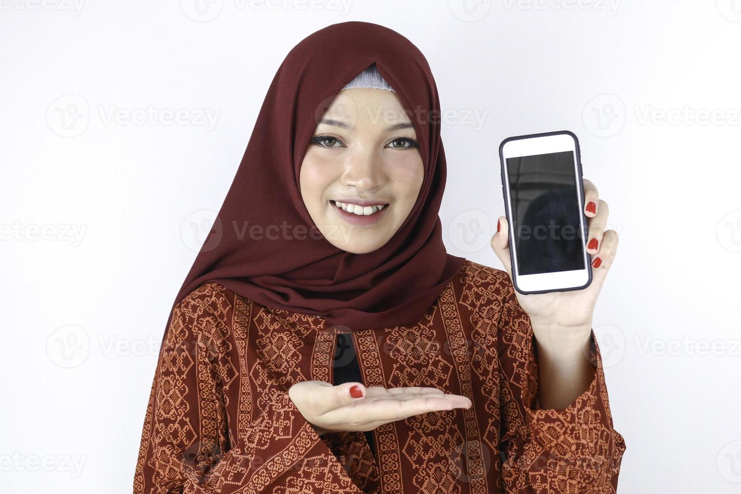 jonge Aziatische islam vrouw lacht wijzend op smartphone staande op een witte achtergrond. foto