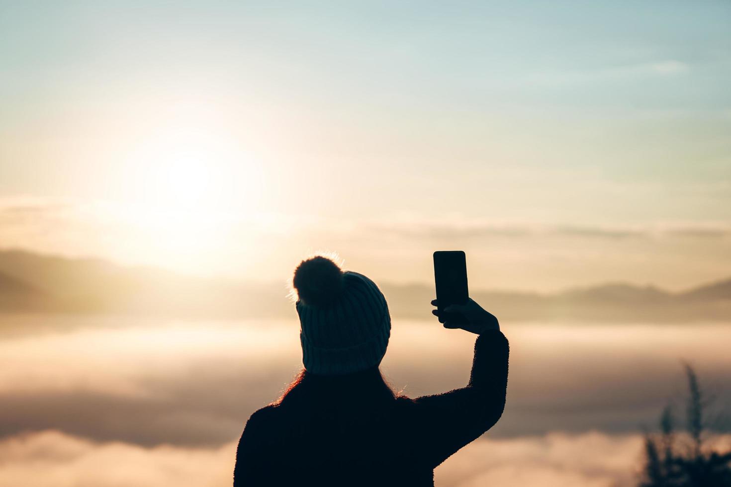 silhouet achteraanzicht van volwassen vrouw ontspannen in de natuur met behulp van mobiele telefoon foto