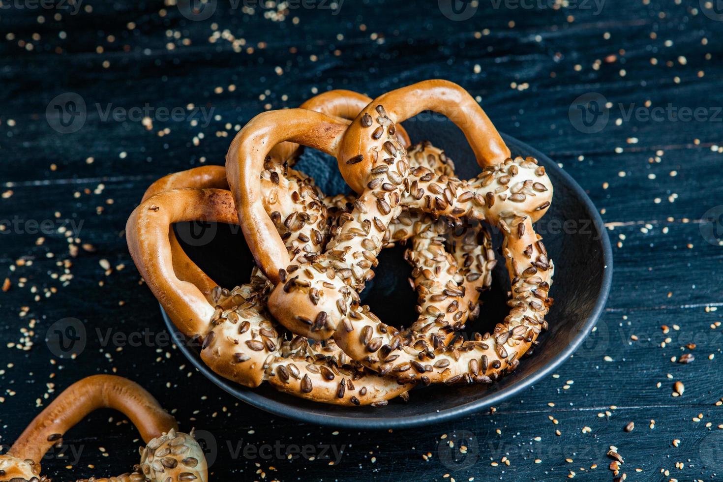 vers bereide zelfgemaakte zachte pretzels. verschillende soorten gebakken bagels met zaden op een zwarte achtergrond. foto