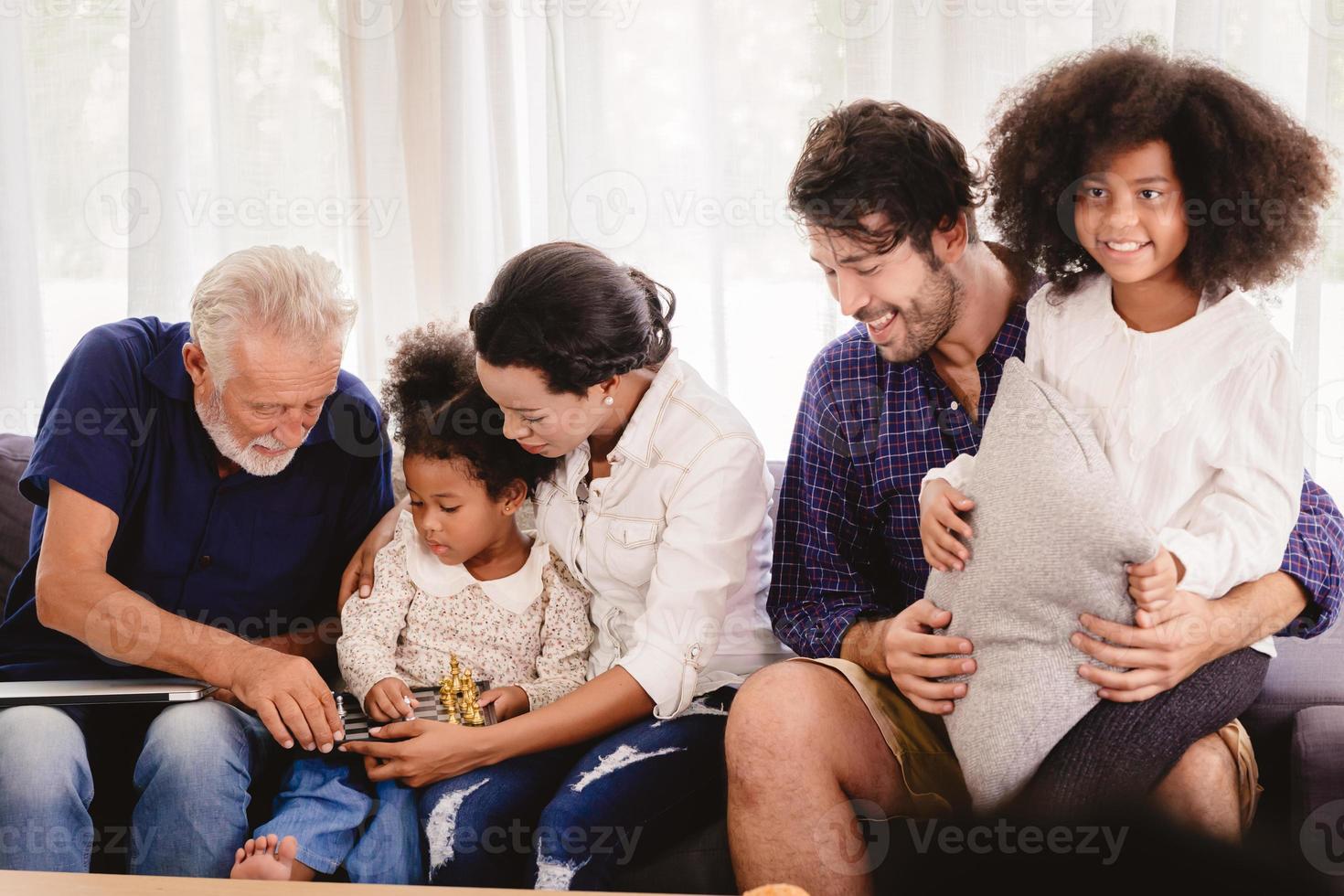 mooie thuis gelukkige familie samenwonen in de woonkamer vader moeder en grootvader spelen met dochter mix race. foto