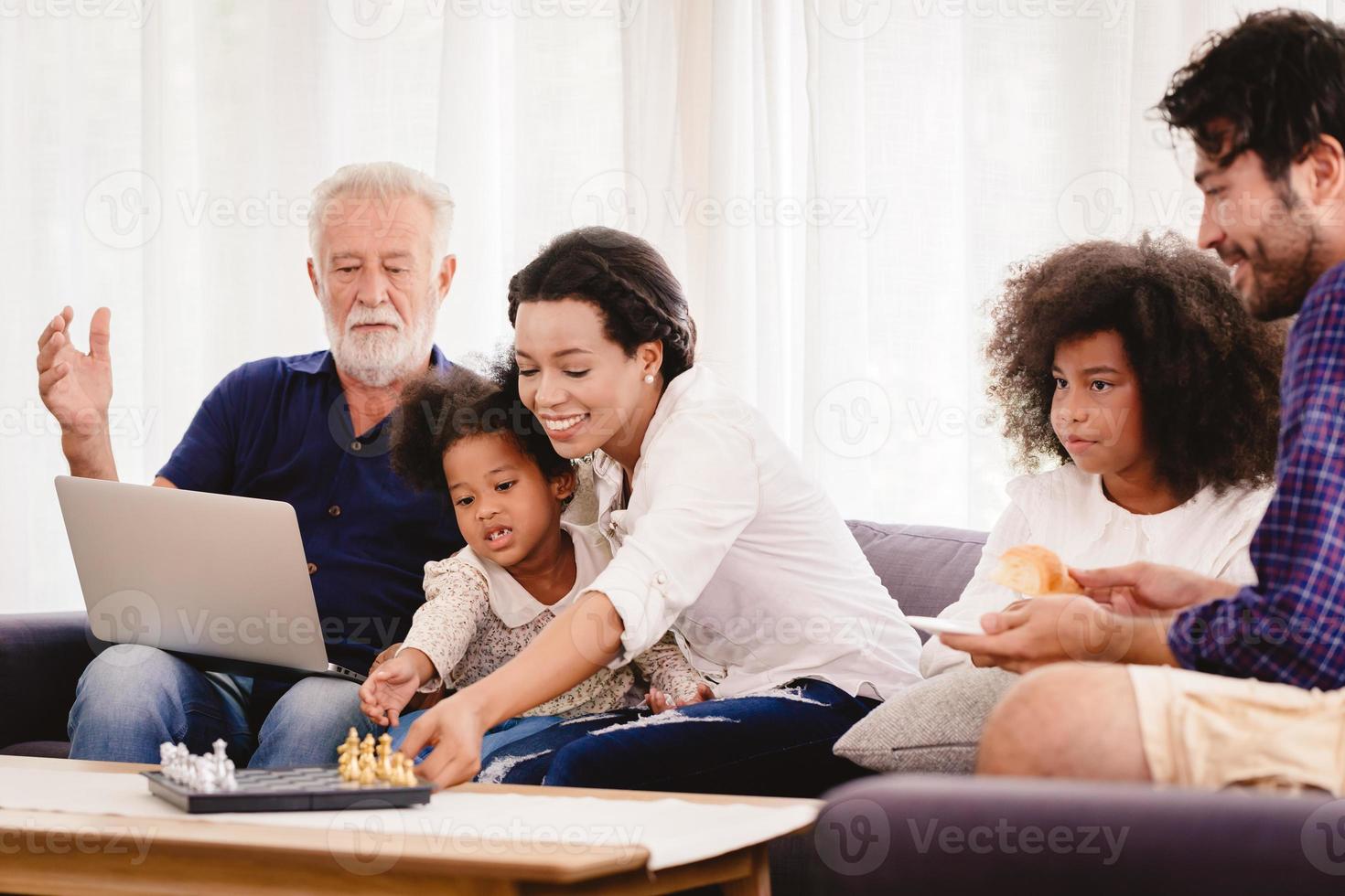 mooie thuis gelukkige familie samenwonen in de woonkamer vader moeder en grootvader spelen met dochter mix race. foto