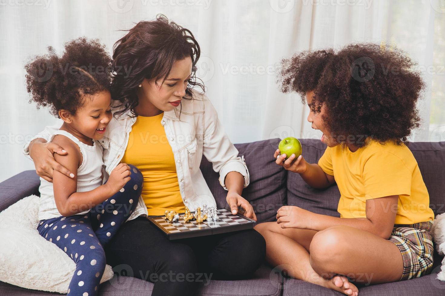 alleenstaande moeder zorgt goed voor haar, leert haar kinderen geniaal te zijn en slimme kleine meisjes die schaakbordspel leren spelen en fruit eten voor gezond. foto