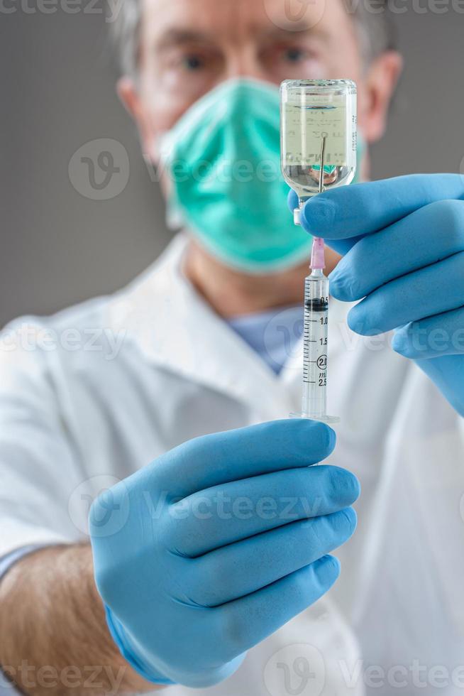 de arts vult een spuit met vaccin op grijze achtergrond. foto