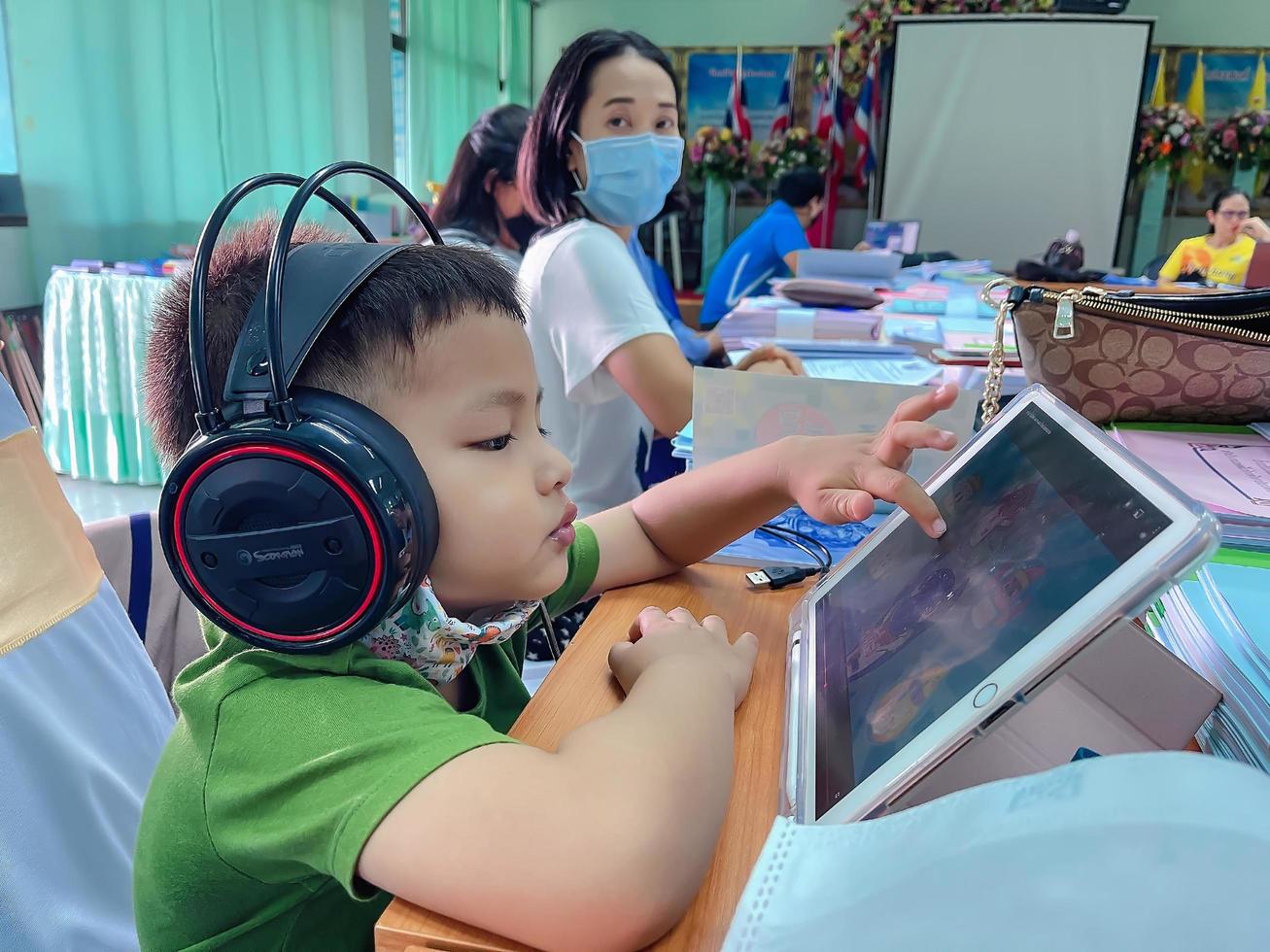 suphan buri, thailand, 10 februari 2021 - kleuterjongen kijkt tekenfilmfilm vanaf tablet terwijl hij wacht op zijn moedervergaderruimte foto