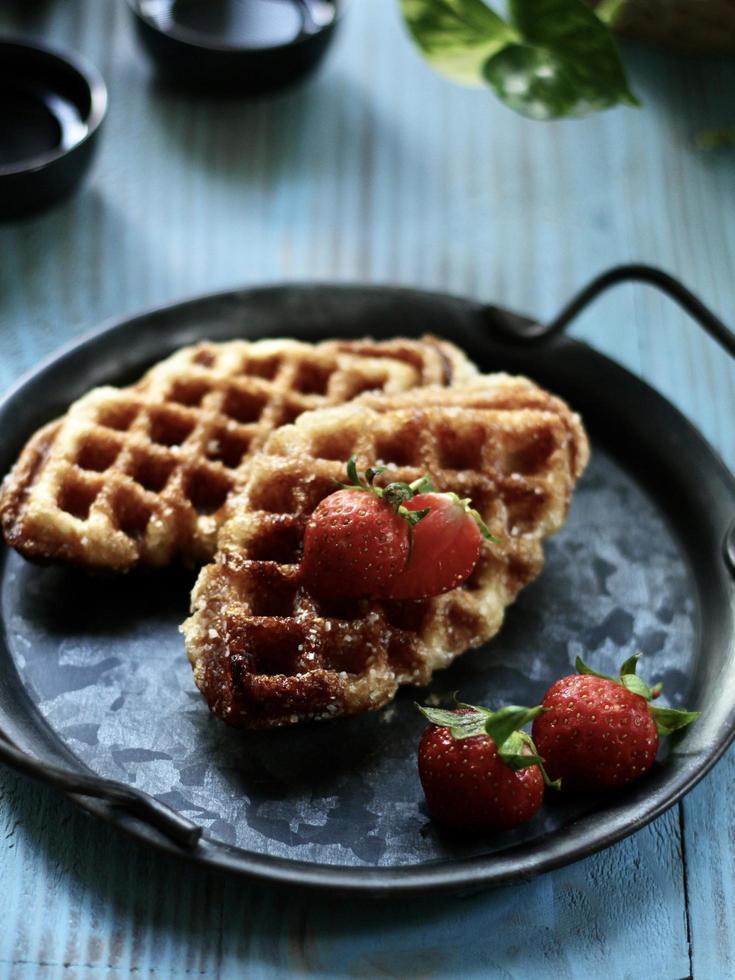 hoge hoekmening van croffle, moderne afhaal- of bezorgmaaltijden, geserveerd met aardbeien op het vintage bord en de blauwe tafel. foto