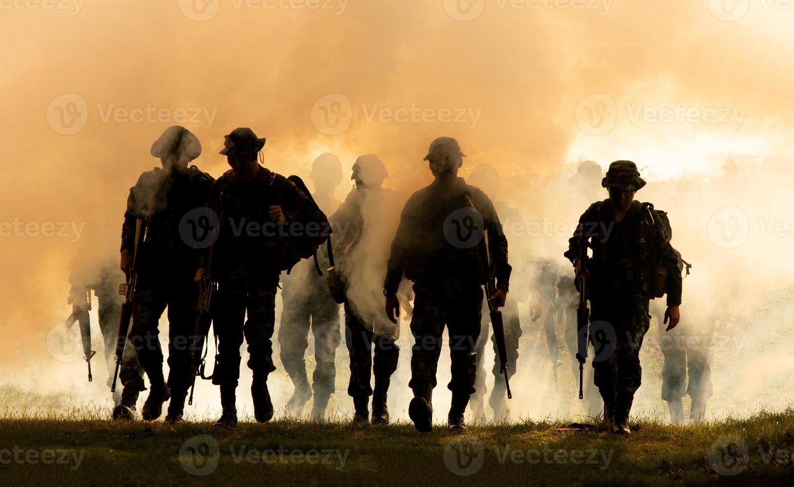 silhouetten van legersoldaten in de mist tegen een zonsondergang, mariniersteam in actie, omringd door vuur en rook, schietend met aanvalsgeweer en machinegeweer, aanvallende vijand foto