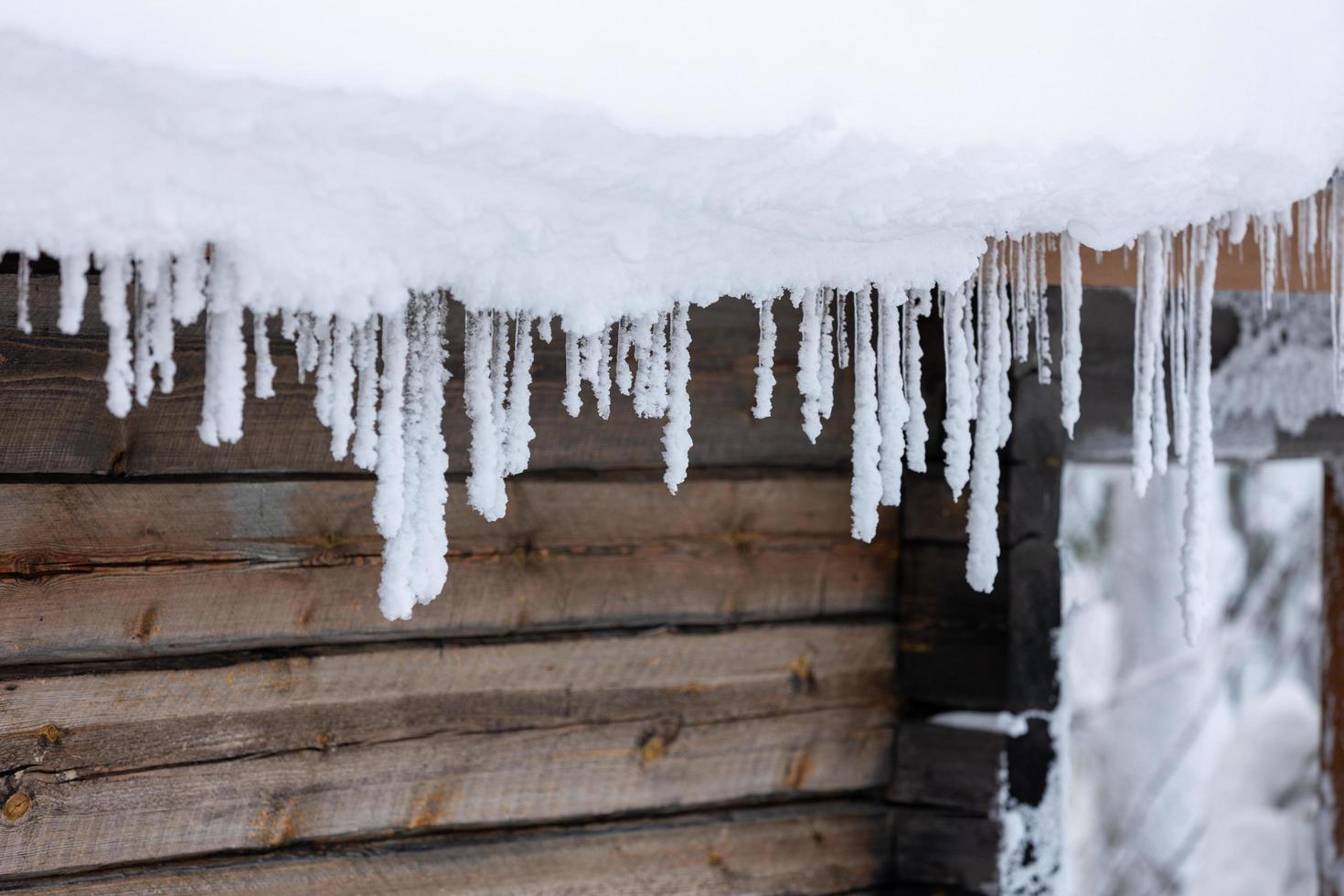 ijspegels onder het besneeuwde dak van een blokhut in de winter in finland. foto