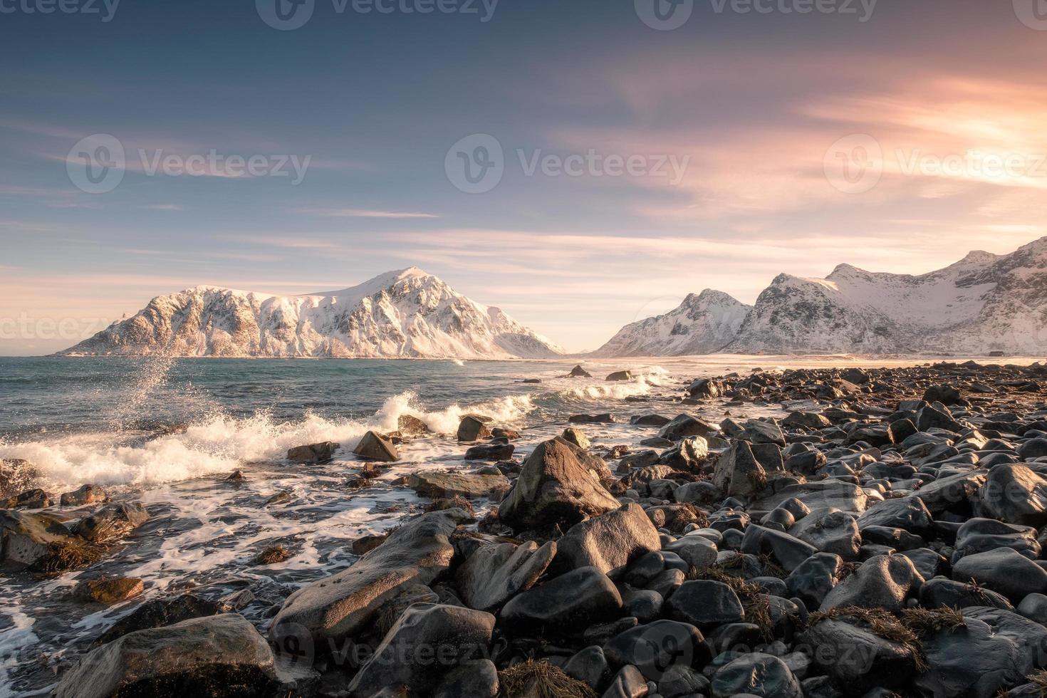 kleurrijke zonsopgang van sneeuwbergketen met golf die op kustlijn bij skagsanden-strand raakt foto