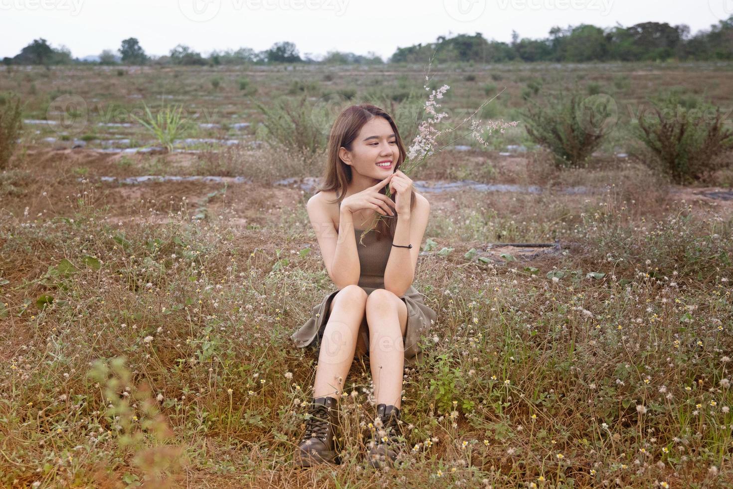 mooie jonge vrouw zittend op het veld in groen gras en paardebloem waait. buitenshuis. geniet van de natuur. gezond glimlachend meisje op de lentegazon. allergievrij concept. vrijheid foto