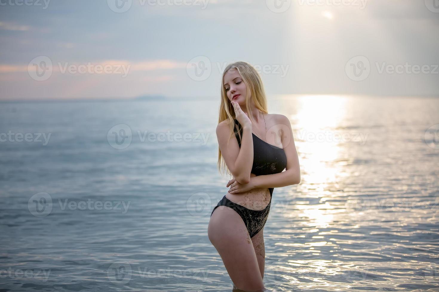 mooie blonde vrouw op zwarte bikini geniet van de zomer op het strand. foto