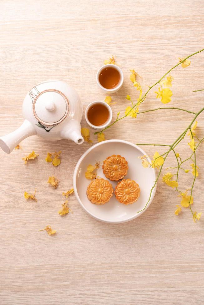 smakelijke maancake voor mid-herfstfestival op heldere houten tafel, concept van feestelijke afternoon tea versierd met gele bloemen, bovenaanzicht, plat gelegd. foto