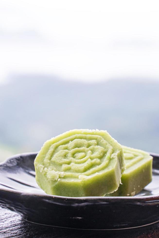 heerlijke groene mungbooncake met zwarte theeplaat op houten balustrade van een theehuis in taiwan met prachtig landschap op de achtergrond, close-up. foto