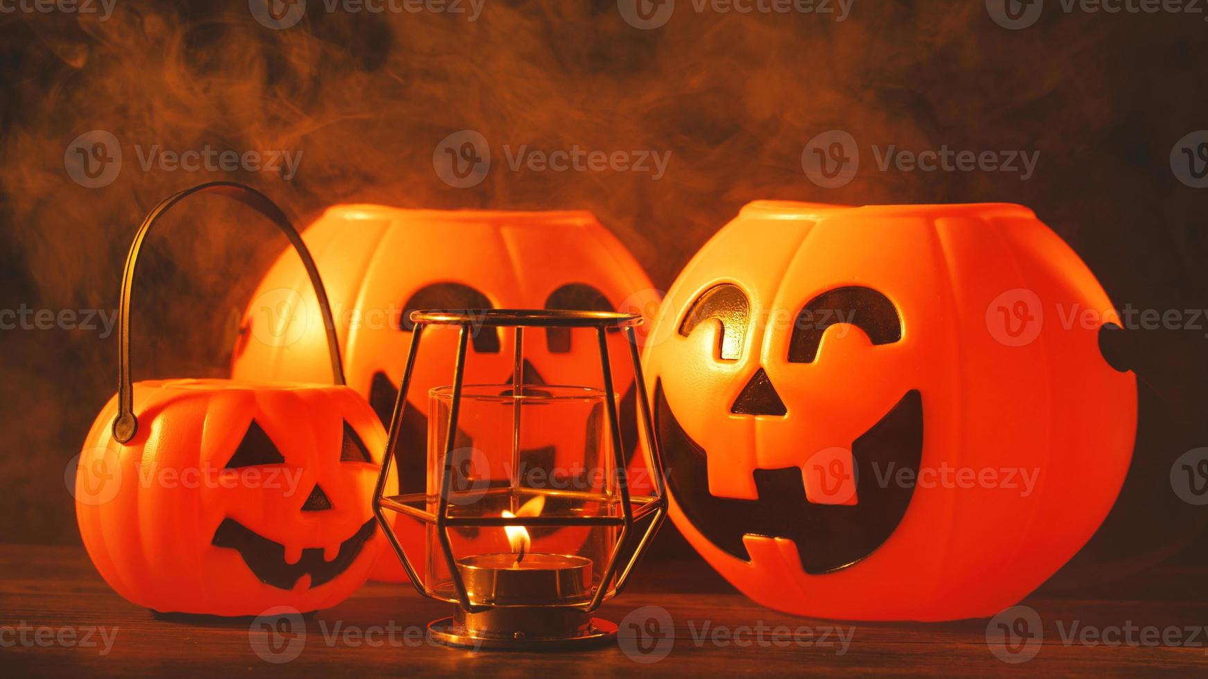 halloween concept - oranje plastic pompoenlantaarn met lachgezicht op een donkere houten tafel met rook rond de achtergrond, trick or treat, close-up. foto