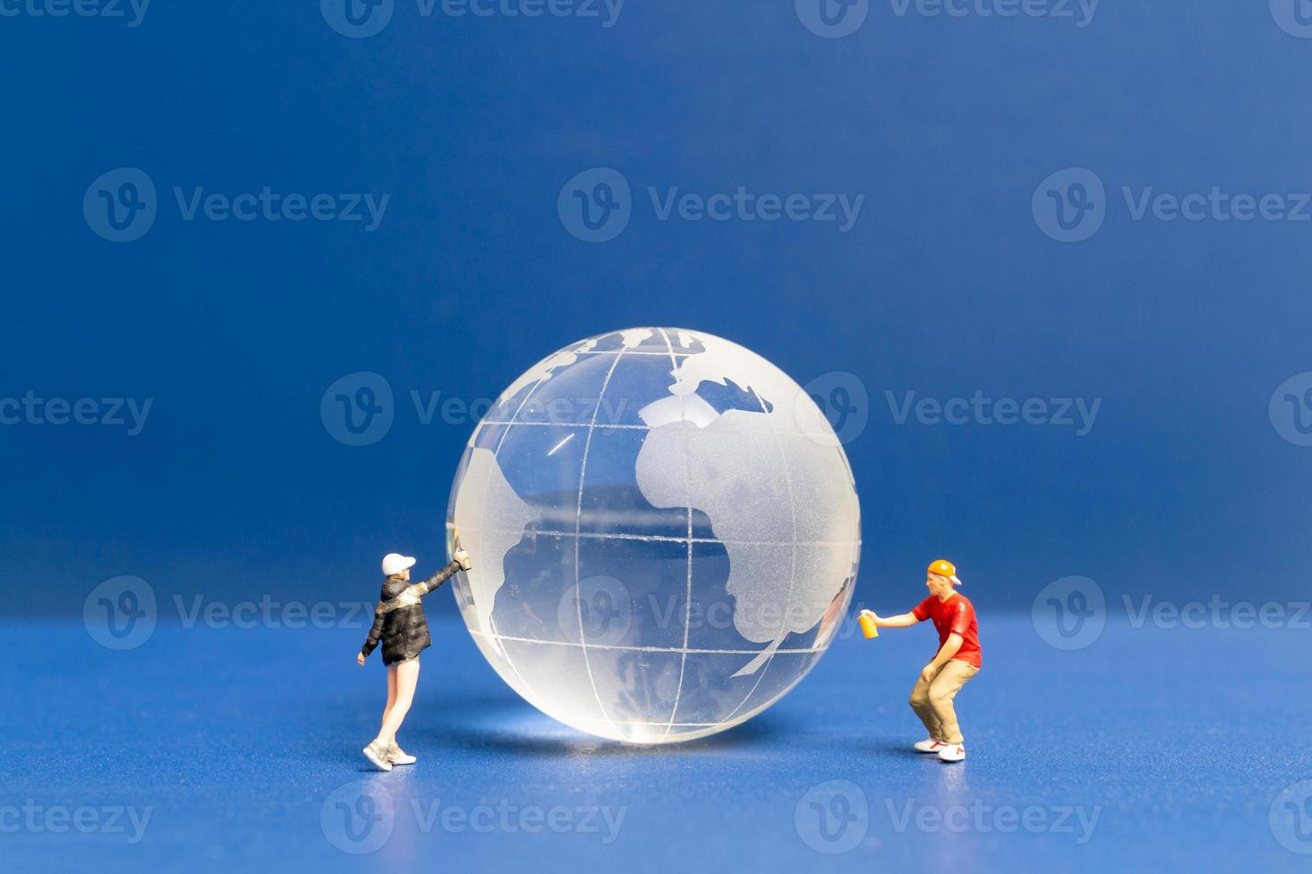 miniatuur mensen tiener spuiten verf crytal globe op blauwe achtergrond foto