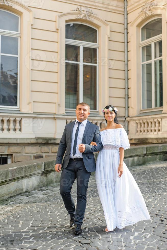 bruiloft fotosessie op de achtergrond van het oude gebouw. de bruidegom kijkt naar zijn bruid die poseert. rustieke of boho huwelijksfotografie. foto