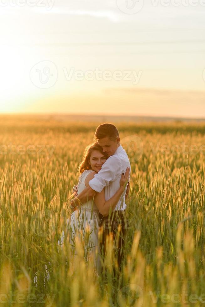 bruid en bruidegom in een tarweveld. het paar knuffelt tijdens zonsondergang foto
